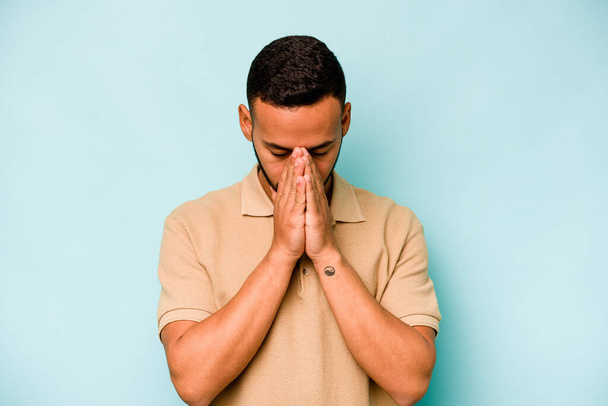 Mladý hispánec izolovaný na modrém pozadí modlící se, projevující oddanost, věřící hledající božskou inspiraci. - Fotografie, Obrázek
