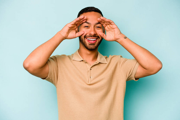 Young hispanic man isolated on blue background receiving a pleasant surprise, excited and raising hands. - 写真・画像