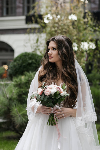 Charming happy bride with long veil. Green park on the background. - Foto, Bild