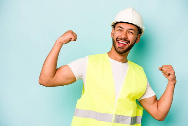 Young laborer hispanic man isolated on blue background raising fist after a victory, winner concept. - Foto, afbeelding