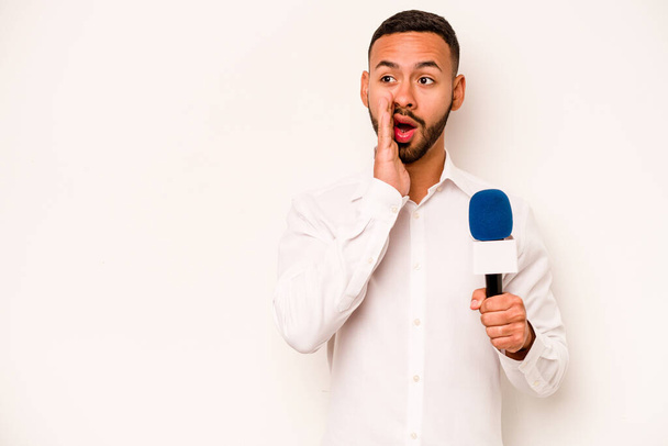 Young hispanic TV presenter isolated on blue background is saying a secret hot braking news and looking aside - Fotografie, Obrázek