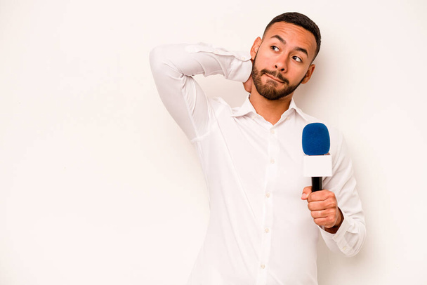Junge hispanische TV-Moderatorin isoliert auf blauem Hintergrund berührt Hinterkopf, denkt nach und trifft eine Wahl. - Foto, Bild