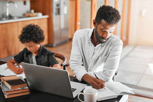 Nur ein alleinerziehender Vater arbeitet von zu Hause aus. Aufnahme eines Mannes, der seinen Laptop benutzt, während er mit seinem Sohn sitzt. - Foto, Bild