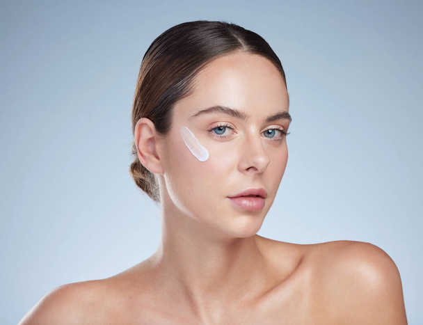For skin that looks effortlessly smooth. Studio portrait of an attractive young woman moisturizing her face against a grey background. - Foto, Imagen