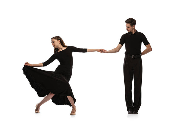 Dynamic portrait of young emotive dancers in black outfits dancing ballroom dance isolated on white background. Concept of art, beauty, music, style. - 写真・画像