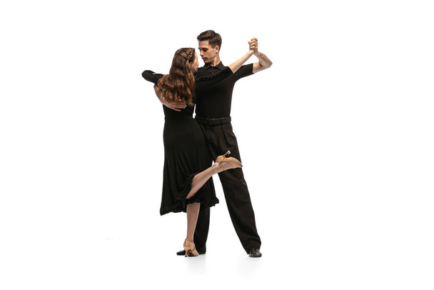 Dynamic portrait of young emotive dancers in black outfits dancing ballroom dance isolated on white background. Concept of art, beauty, music, style. - Photo, image