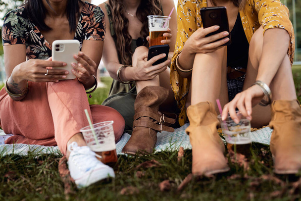 Çimlerin üzerinde oturan ve cep telefonu tutan kadınların düşük kesimi - Fotoğraf, Görsel