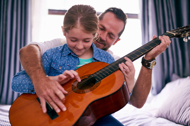 Μουσικός δεσμός. Τραβηγμένο πλάνο ενός πατέρα και της κόρης παίζει κιθάρα μαζί στο σπίτι. - Φωτογραφία, εικόνα