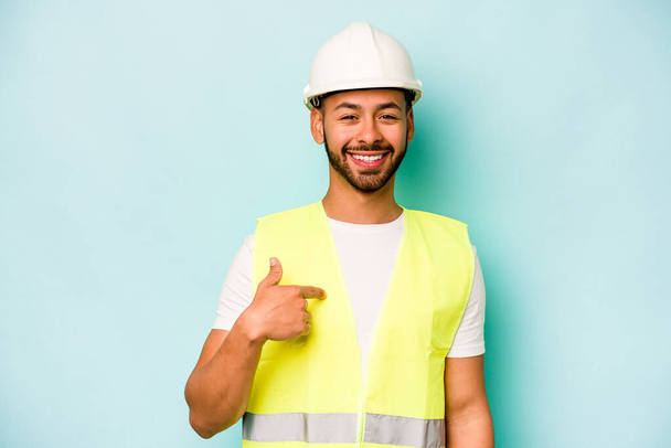 Jeune ouvrier hispanique homme isolé sur fond bleu personne pointant à la main vers un espace de copie chemise, fier et confiant - Photo, image