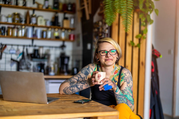 Tetovált nő tolószékben dolgozik laptop otthon - Fotó, kép