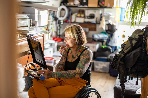 Young woman in a wheelchair doing her make-up at home - 写真・画像