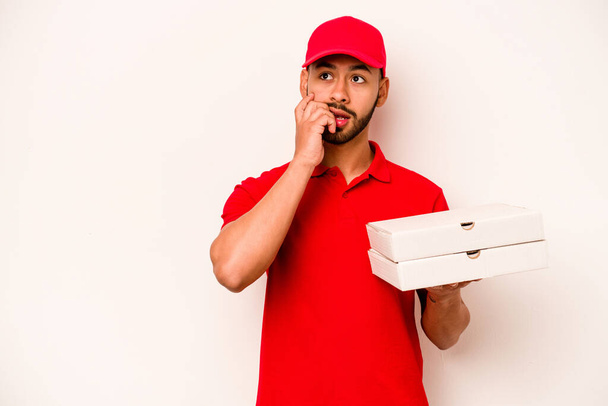 Jeune livreur hispanique tenant des pizzas isolées sur fond blanc détendu penser à quelque chose en regardant un espace de copie. - Photo, image