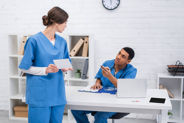 Vet doctor holding scan near blurred african american colleague with clipboard in clinic  - Foto, imagen