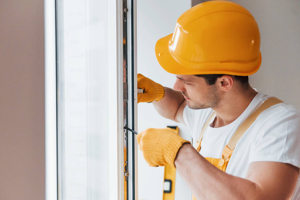 Handyman in yellow uniform installs new window. House renovation conception. - Foto, afbeelding