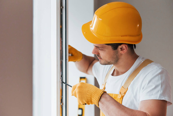 Handyman in yellow uniform installs new window. House renovation conception. - 写真・画像