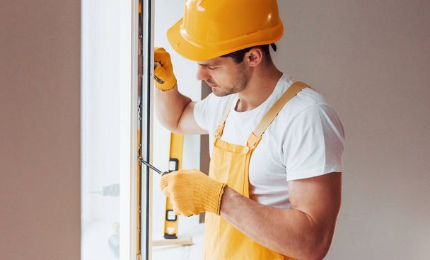 Handyman in yellow uniform installs new window. House renovation conception. - Фото, зображення