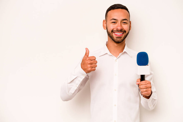 Young hispanic TV presenter isolated on blue background smiling and raising thumb up - Фото, изображение