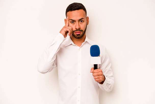 Joven presentador de televisión hispana aislado sobre fondo azul apuntando templo con el dedo, pensando, enfocado en una tarea. - Foto, imagen