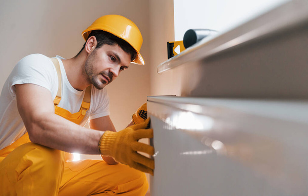 Handyman in yellow uniform installing new battery. House renovation conception. - Фото, изображение
