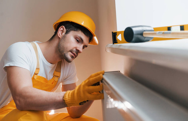 Handyman in yellow uniform installing new battery. House renovation conception. - Φωτογραφία, εικόνα