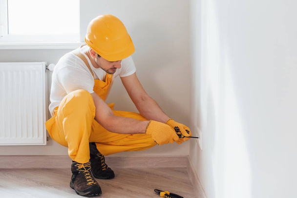 Handyman in yellow uniform works with electricity and installing new socket. House renovation conception. - Fotografie, Obrázek