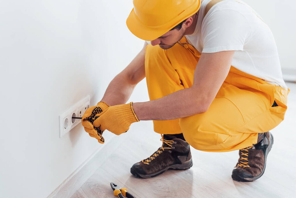 Handyman in yellow uniform works with electricity and installing new socket. House renovation conception. - Valokuva, kuva