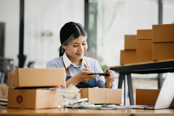 A woman using a smartphone to take pictures in front of parcel boxes, parcel boxes for packing goods, delivering goods through private courier companies. Online selling and online shopping concepts. - Zdjęcie, obraz