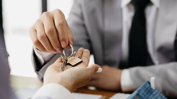 Egy lakásbérlő cég alkalmazottja átadja a ház kulcsait egy ügyfélnek, aki beleegyezett, hogy aláírja a bérleti szerződést, elmagyarázva a bérleti szerződés részleteit és feltételeit. Lakás- és ingatlanbérleti ötletek. - Fotó, kép
