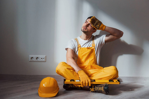Tired handyman in yellow uniform sits indoors and takes break. House renovation conception. - Valokuva, kuva