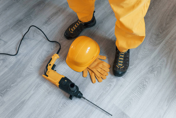 Handyman in yellow uniform with drill standing indoors. House renovation conception. - Fotografie, Obrázek