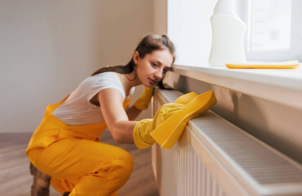 Housewife in yellow uniform works with window and surface cleaner indoors. House renovation conception. - Fotoğraf, Görsel