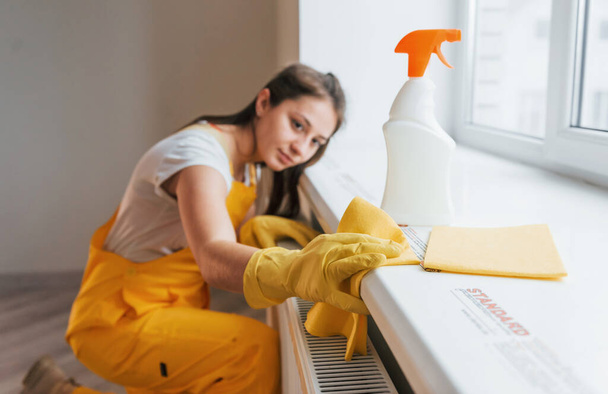 Housewife in yellow uniform works with window and surface cleaner indoors. House renovation conception. - 写真・画像