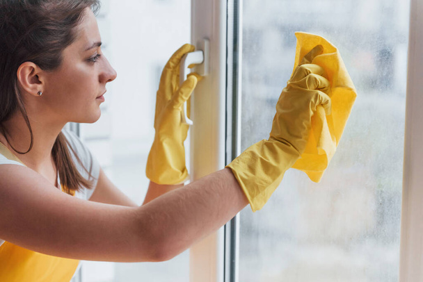 Housewife in yellow uniform cleaning windows. House renovation conception. - Foto, afbeelding