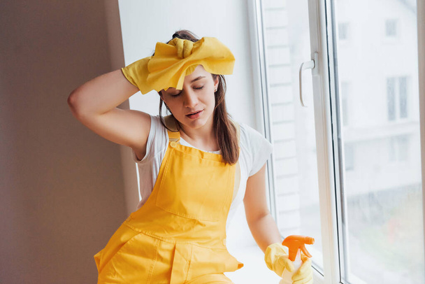 Tired housewife in yellow uniform takes a break indoors. House renovation conception. - Foto, immagini
