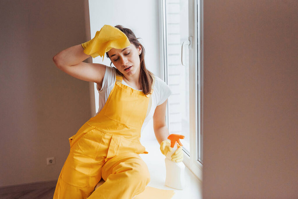 Tired housewife in yellow uniform takes a break indoors. House renovation conception. - Foto, afbeelding