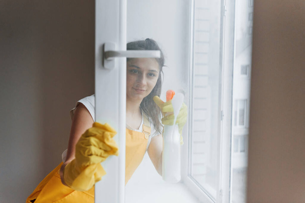Housewife in yellow uniform cleaning windows. House renovation conception. - Foto, afbeelding
