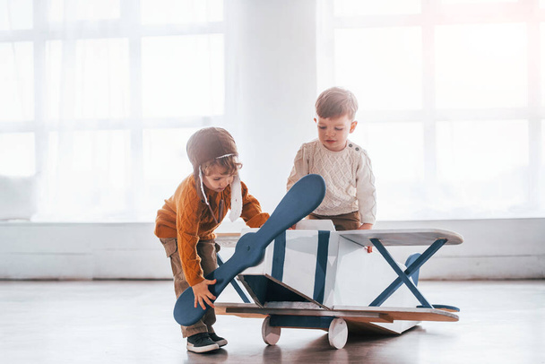 Two little boys in retro pilot uniform having fun with toy plane indoors. - Photo, image