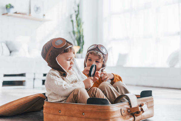 Two little boys have fun and sitting in suitcase indoors at daytime. - Foto, immagini