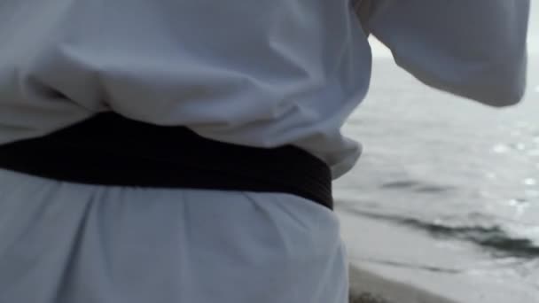 Strong man exercising karate punches close up. Sportsman training on sandy beach - Filmati, video