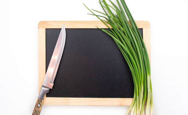 Green onion and knife on cutting black board on isolated background. Ingredient, preparation. Copy space - Photo, image