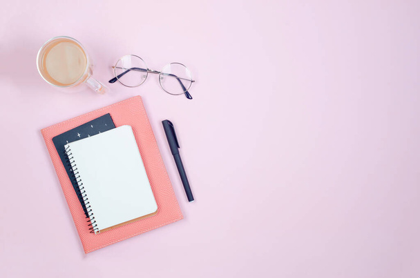 Flat lay, office table top view. Workspace desk with empty blank, supplies, glasses and coffee cups on pink background. Minimal style home office or Modern freelancer workspace. - Fotó, kép