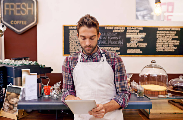 De nieuwste koffietrends bekijken. Foto van een jonge barista met behulp van een digitale tablet in een café. - Foto, afbeelding