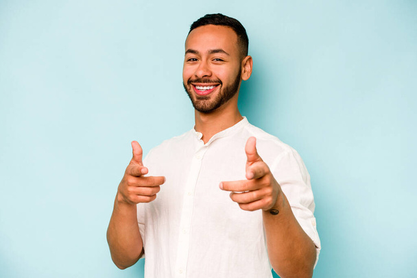 Young hispanic man isolated on blue background cheerful smiles pointing to front. - Фото, изображение