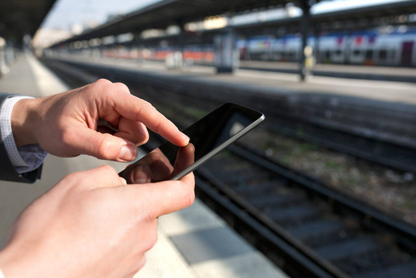 Man using a mobile phone on empty railway platform. Close-up hands - Φωτογραφία, εικόνα
