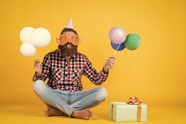 happy handsome bearded guy with unshaven face and stylish hairdo wear casual clothes holding present and party balloons, birthday holiday - Fotó, kép