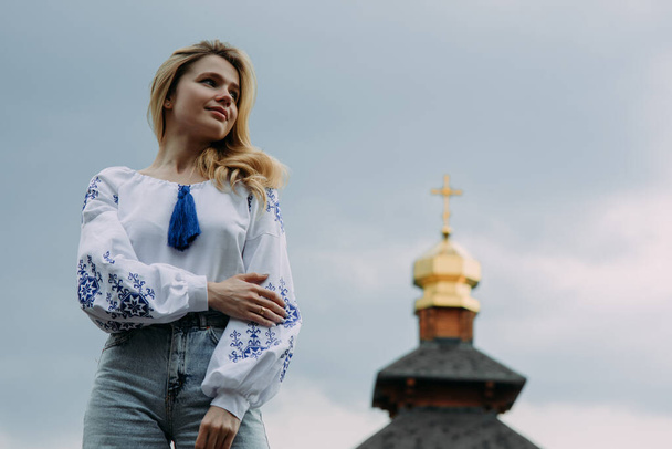 Fiatal szőke nő áll az ukrán nemzeti hímzett ing ellen háttér elmosódott arany templom kupola kereszt és az ég. - Fotó, kép