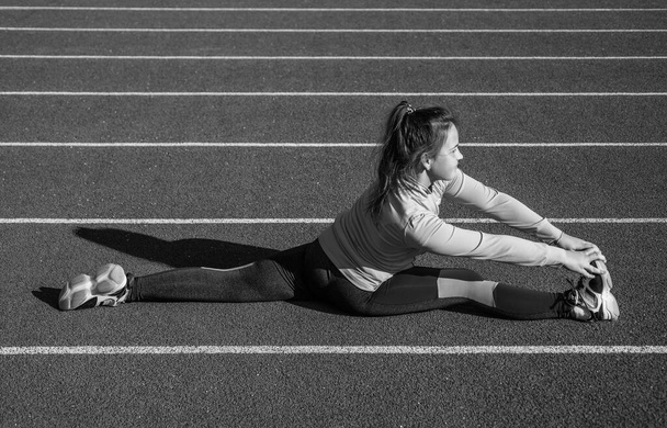 Doing her best. healthy childhood. workout on fresh air outdoor. confident runner. flexible body. teen girl warm up on stadium. kid in sportswear stretching. child do split exercise on racing track - Fotó, kép