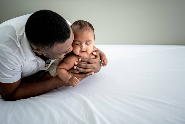 African father hugging and protect his daughter, 3 month old baby newborn which is smiling and happy in a white bedroom,  to African family and newborn concept. - Foto, Imagem