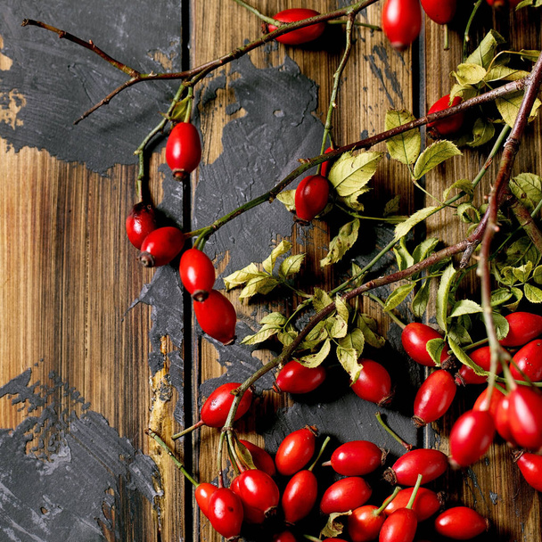 Rose hip berries with branch and leaves on old wooden plank background. Autumn reserves of vitamins for the winter. Flat lay. Square image - Фото, изображение