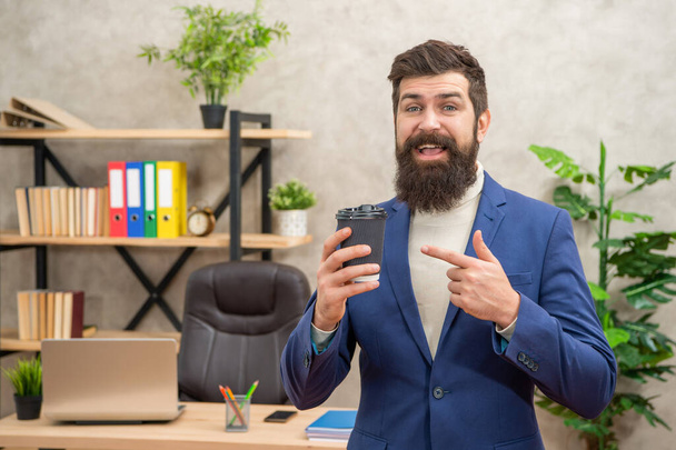 smiling business man point finger on takeaway coffee in the office with copy space, coffee break. - Foto, Bild
